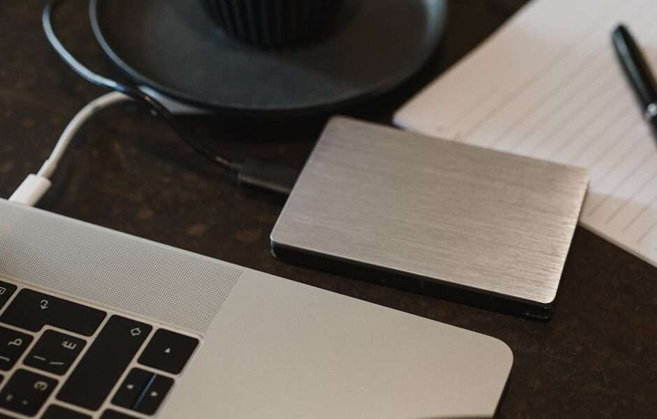 Laptop podłączony kablem do zewnętrznego srebrnego dysku twardego na biurku.
