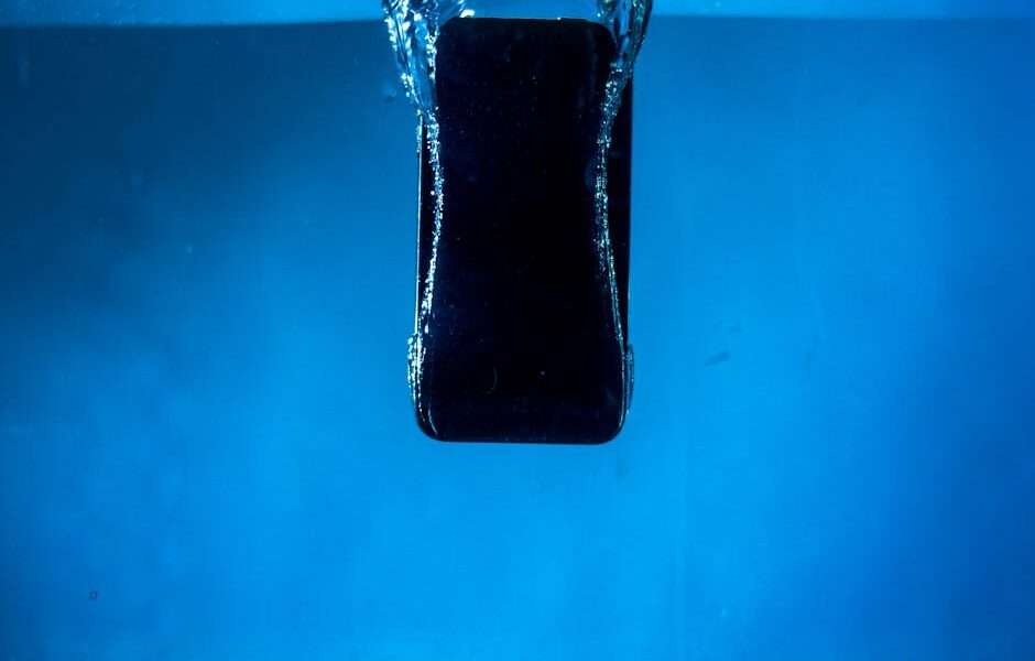 Smartfon zanurzający się w przezroczystej wodzie na tle niebieskiego koloru.