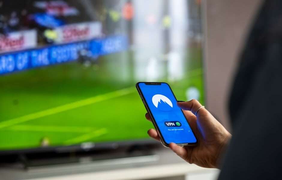 kobieta trzymająca w ręku telefon z VPN, w tle telewizor z transmisją meczu
