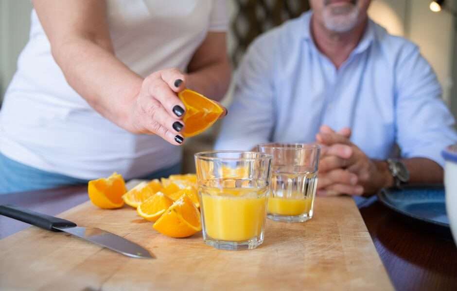 para przygotowująca sok pomarańczowy, szklanki z sokiem, pokrojone pomarańcze