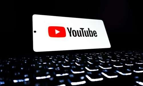 Telefon z logo YouTube położony na podświetlanej klawiaturze laptopa.