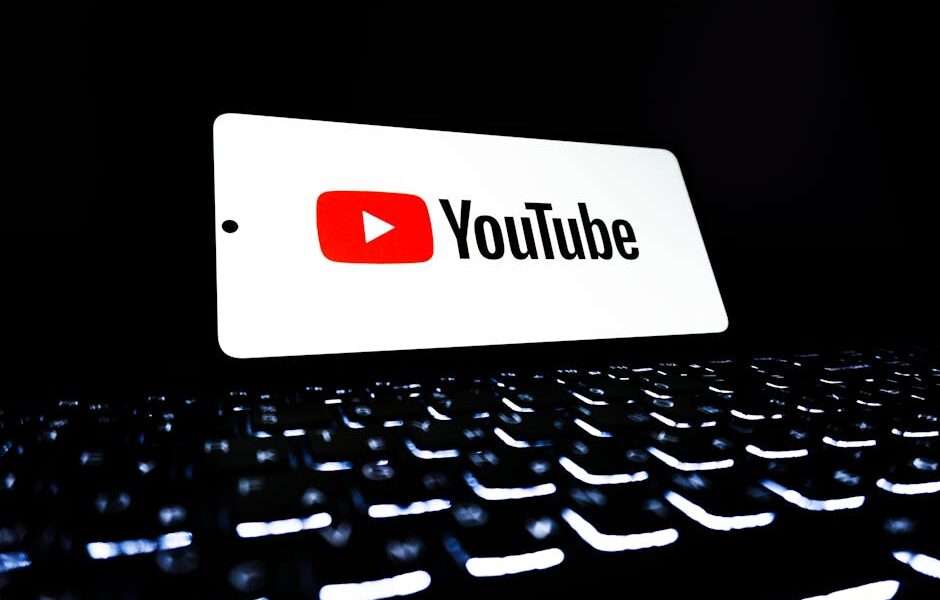 Telefon z logo YouTube położony na podświetlanej klawiaturze laptopa.